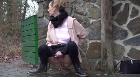 White girl Cynthia Vellons takes a piss on a deck behind a stone structure 52368304